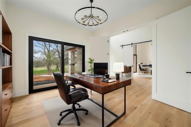 office space with an inviting chandelier, a barn door, and light hardwood / wood-style floors