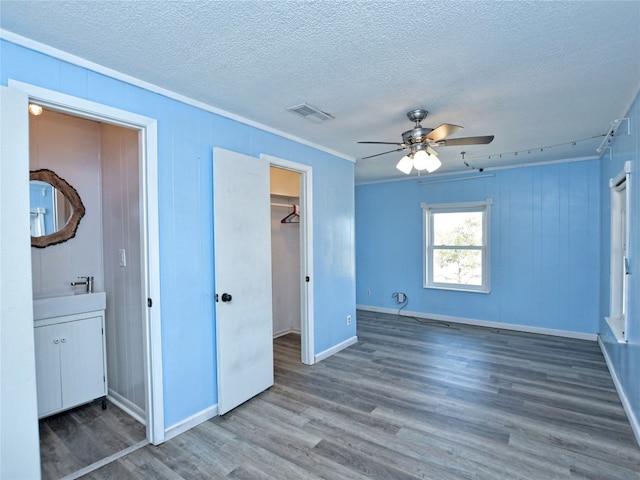 unfurnished bedroom with ceiling fan, a closet, a textured ceiling, a walk in closet, and dark hardwood / wood-style floors