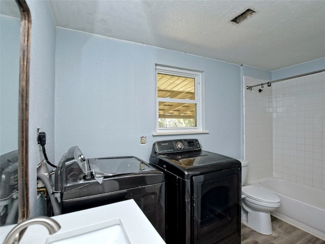 clothes washing area with a textured ceiling, wood-type flooring, independent washer and dryer, and sink