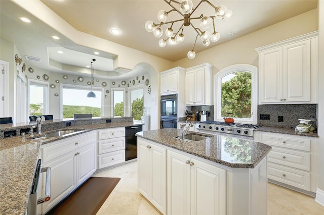 kitchen featuring sink, a raised ceiling, hanging light fixtures, backsplash, and a center island with sink