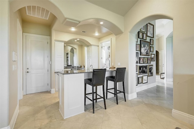 kitchen featuring kitchen peninsula, a breakfast bar, dark stone countertops, and light tile floors