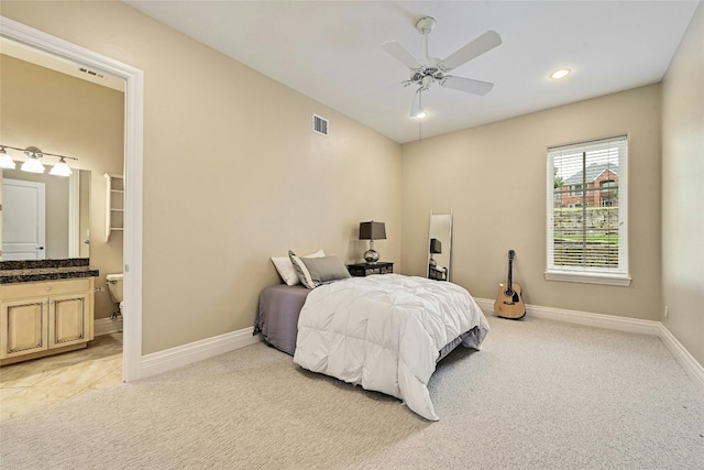 bedroom with ensuite bathroom, light colored carpet, and ceiling fan