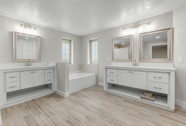 bathroom featuring a tub, double vanity, and a textured ceiling