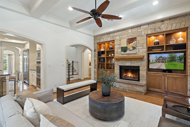 living room with ceiling fan, a fireplace, beam ceiling, light hardwood / wood-style flooring, and built in shelves