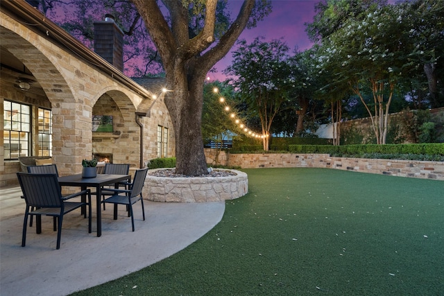 patio terrace at dusk with an outdoor stone fireplace and a yard