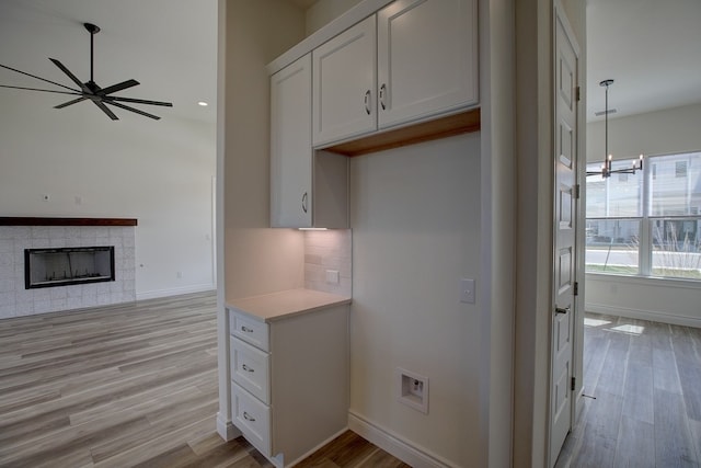 kitchen with backsplash, a fireplace, light wood-type flooring, and white cabinets