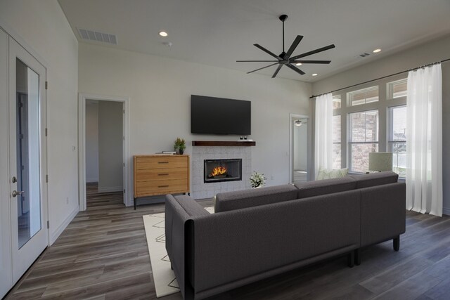 living room featuring dark wood-type flooring, ceiling fan, and a tile fireplace