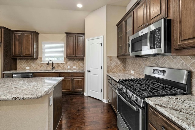 kitchen with appliances with stainless steel finishes, light stone counters, backsplash, dark hardwood / wood-style flooring, and sink