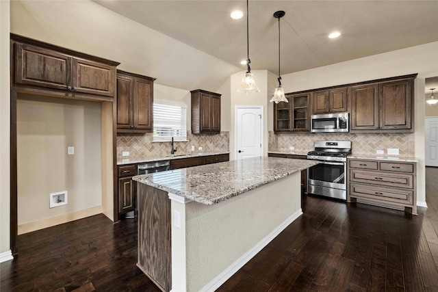 kitchen featuring decorative light fixtures, dark wood-type flooring, stainless steel appliances, light stone counters, and a kitchen island