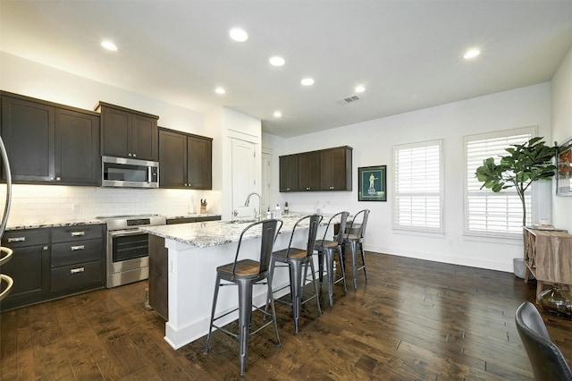 kitchen featuring a center island with sink, dark wood-type flooring, range, and light stone counters