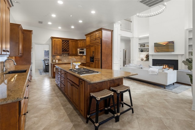 kitchen with built in features, a kitchen island, stainless steel appliances, light stone counters, and sink