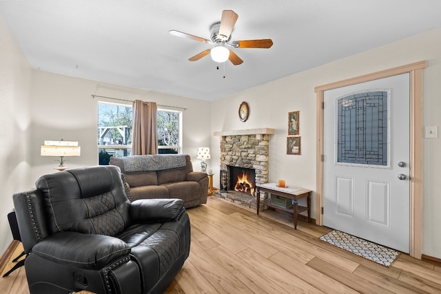 living room featuring a fireplace, ceiling fan, and light wood-type flooring