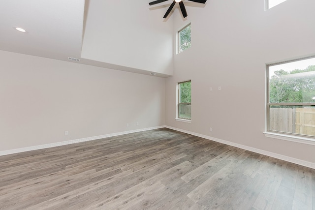 empty room featuring a towering ceiling, a healthy amount of sunlight, light hardwood / wood-style floors, and ceiling fan