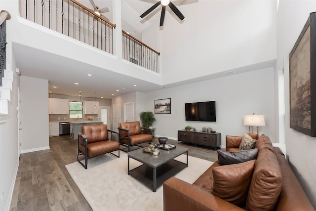 living room featuring ceiling fan, sink, light hardwood / wood-style flooring, and a towering ceiling