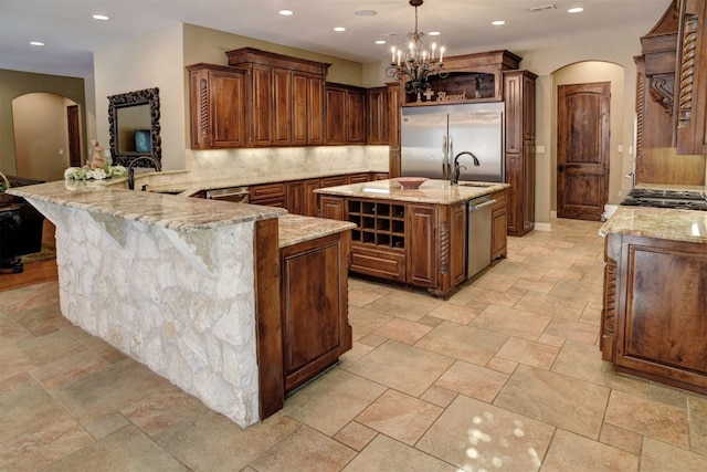 kitchen featuring light stone countertops, decorative light fixtures, backsplash, a kitchen island with sink, and stainless steel appliances