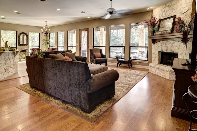 living room with a stone fireplace, light hardwood / wood-style floors, and ceiling fan with notable chandelier