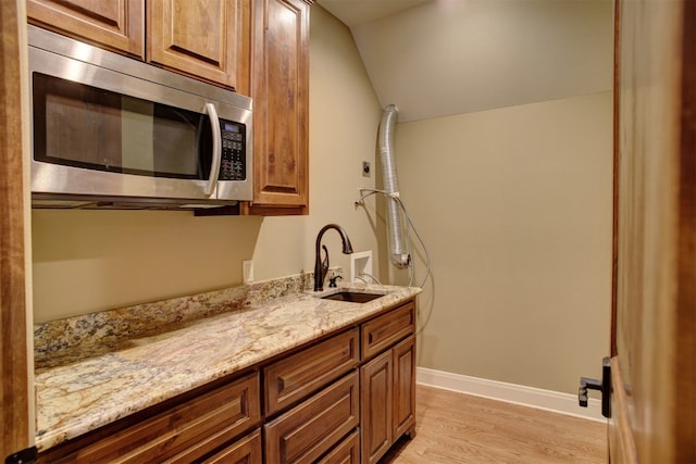 kitchen featuring light hardwood / wood-style floors, vaulted ceiling, light stone countertops, and sink