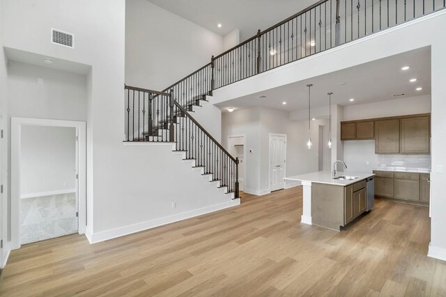 kitchen featuring a kitchen island with sink, hanging light fixtures, sink, a towering ceiling, and light wood-type flooring