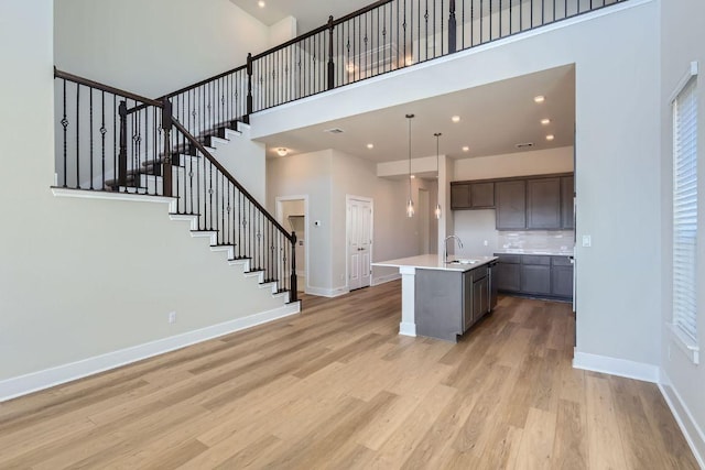 316 Chaste Tree Dr, San Marcos, TX 78666 - kitchen featuring a towering ceiling, a sink, a kitchen island with sink, baseboards, and light wood-type flooring