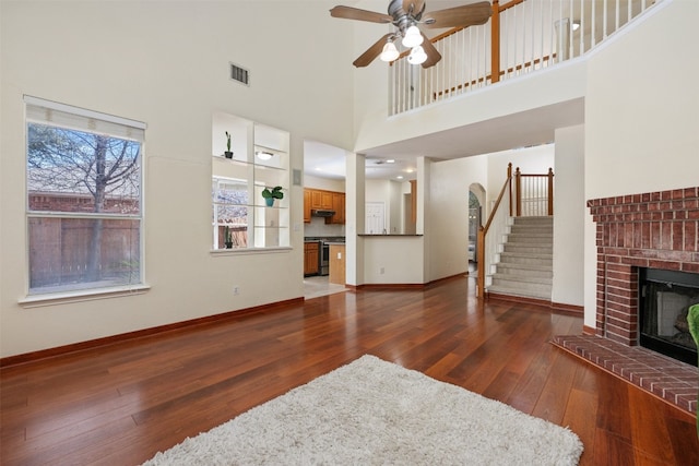 living room with dark hardwood / wood-style floors, ceiling fan, a towering ceiling, and a fireplace