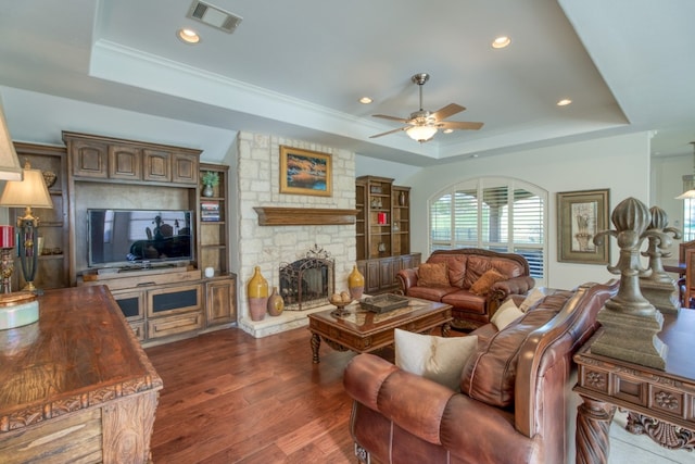 living room with a tray ceiling, a stone fireplace, ceiling fan, and dark hardwood / wood-style floors