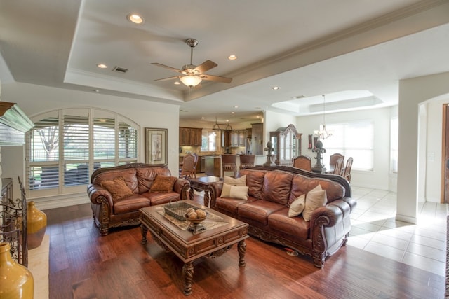 living room with a tray ceiling, hardwood / wood-style floors, ceiling fan with notable chandelier, and ornamental molding