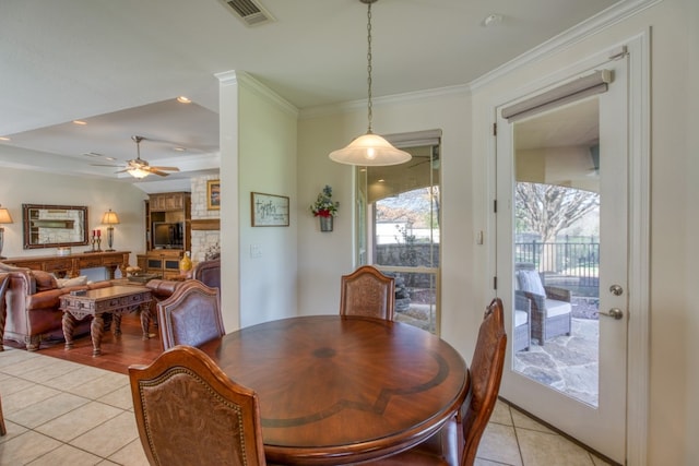 dining space featuring light tile patterned floors, a stone fireplace, ceiling fan, and ornamental molding