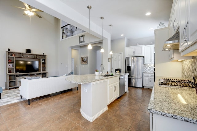 kitchen with sink, an island with sink, stainless steel appliances, decorative light fixtures, and ventilation hood