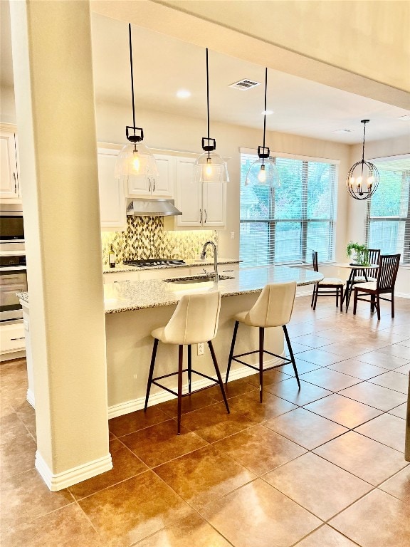 kitchen with light stone counters, appliances with stainless steel finishes, a kitchen bar, and white cabinets