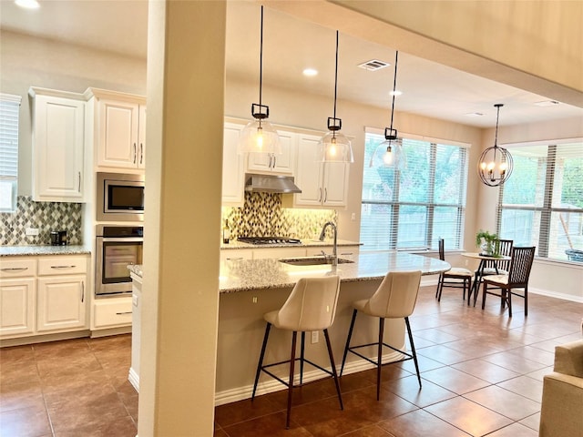 kitchen with light stone countertops, sink, stainless steel appliances, decorative light fixtures, and a breakfast bar