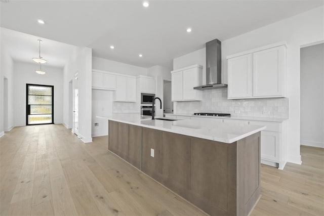 kitchen featuring white cabinets, wall chimney range hood, a large island with sink, and light hardwood / wood-style flooring