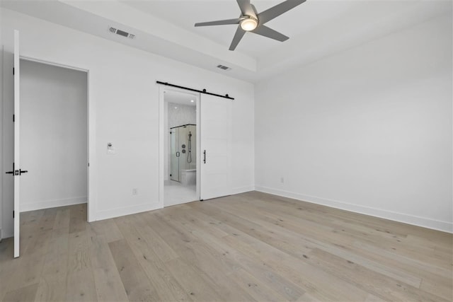 unfurnished bedroom with a barn door, ceiling fan, ensuite bath, and light wood-type flooring