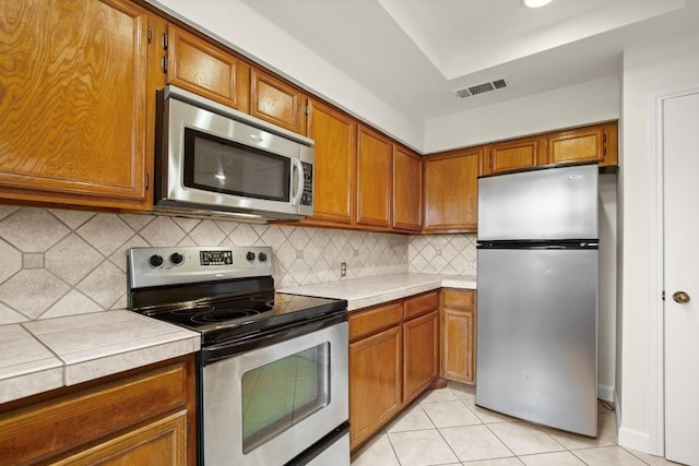 kitchen featuring light tile patterned floors, backsplash, tile counters, and appliances with stainless steel finishes