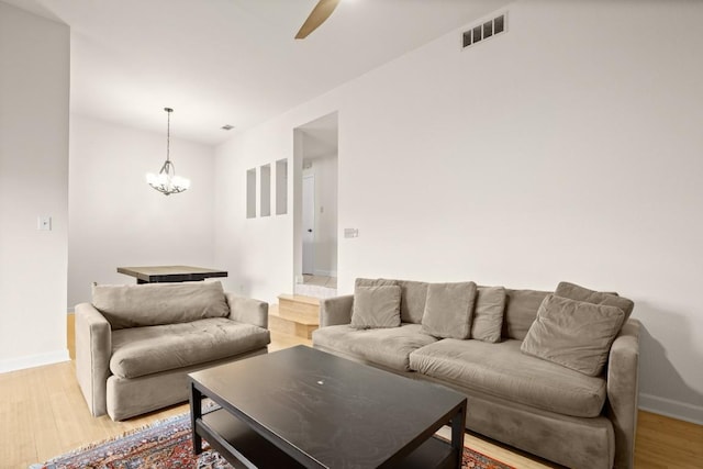 living room with ceiling fan with notable chandelier and light hardwood / wood-style flooring