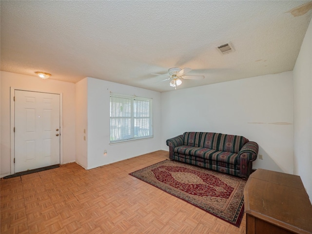 living room with ceiling fan, light parquet floors, and a textured ceiling