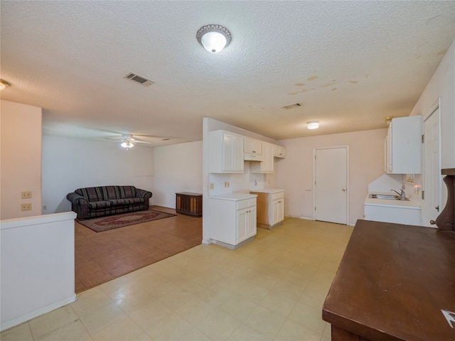 kitchen with a textured ceiling, ceiling fan, white cabinets, and light tile flooring