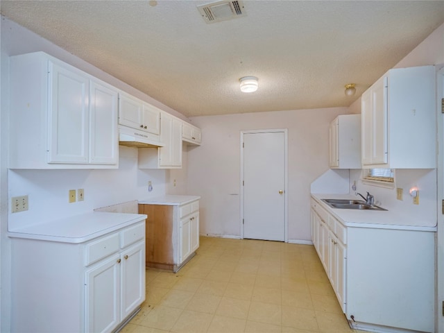 kitchen featuring white cabinets, a textured ceiling, sink, and light tile flooring