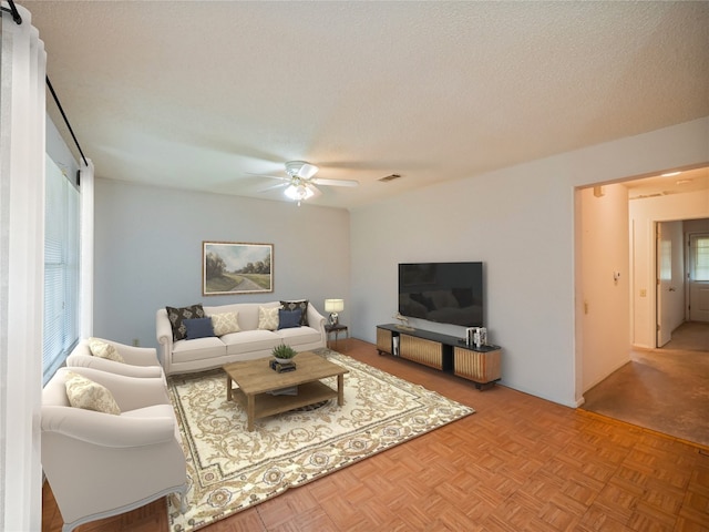 living room with ceiling fan, a textured ceiling, and light parquet flooring