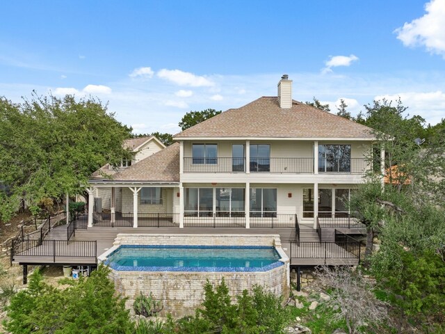 rear view of house featuring a swimming pool with hot tub and a balcony