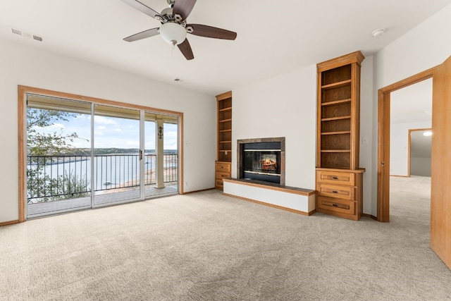 unfurnished living room with a water view, light colored carpet, built in features, and ceiling fan