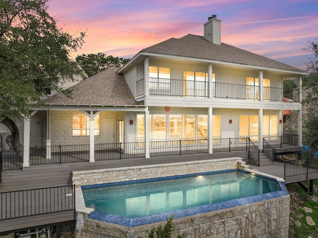 back house at dusk featuring a fenced in pool and a balcony