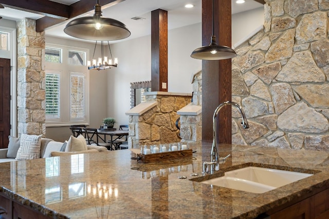 kitchen with a chandelier, pendant lighting, beamed ceiling, dark stone countertops, and sink