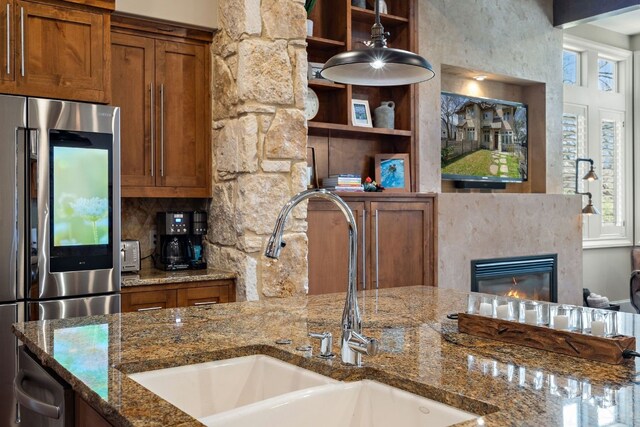 kitchen featuring stainless steel appliances, sink, dark stone countertops, and a stone fireplace