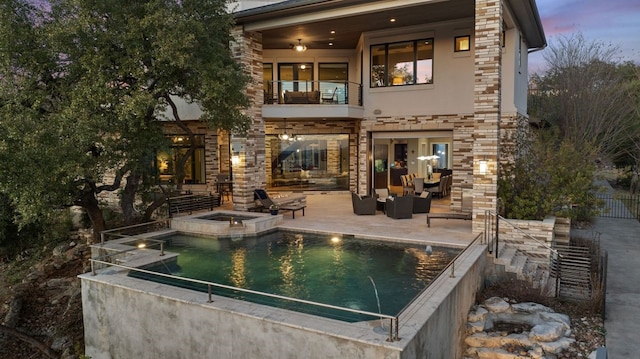 back house at dusk featuring an outdoor living space, a pool with hot tub, a patio area, and a balcony