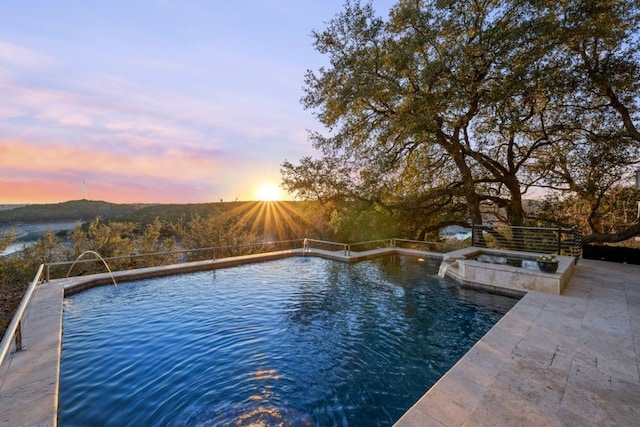 pool at dusk with an in ground hot tub, pool water feature, and a patio area