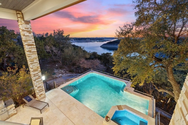 pool at dusk with a patio area, a water view, and an in ground hot tub