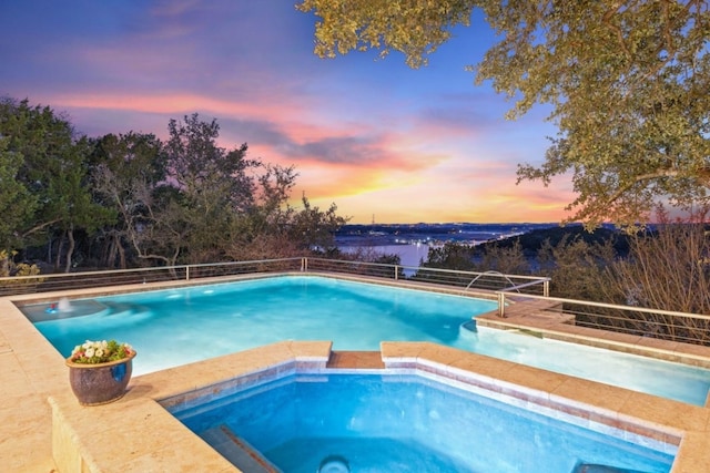 pool at dusk featuring an in ground hot tub