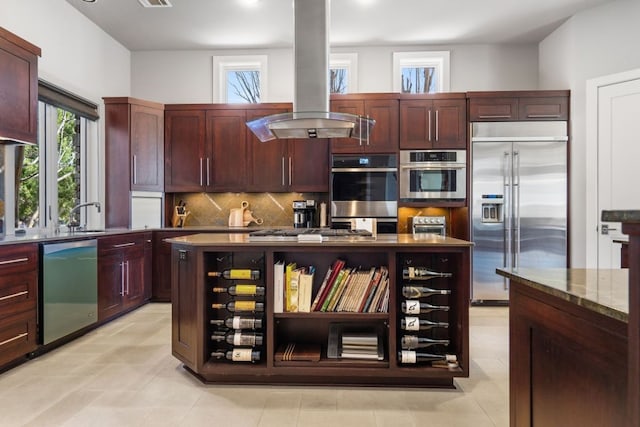 kitchen featuring appliances with stainless steel finishes, backsplash, island range hood, a kitchen island, and light tile patterned flooring