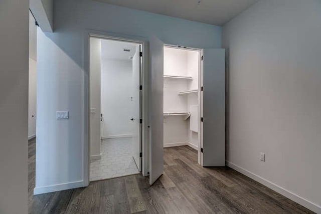 unfurnished bedroom with dark wood-type flooring, a spacious closet, and a closet