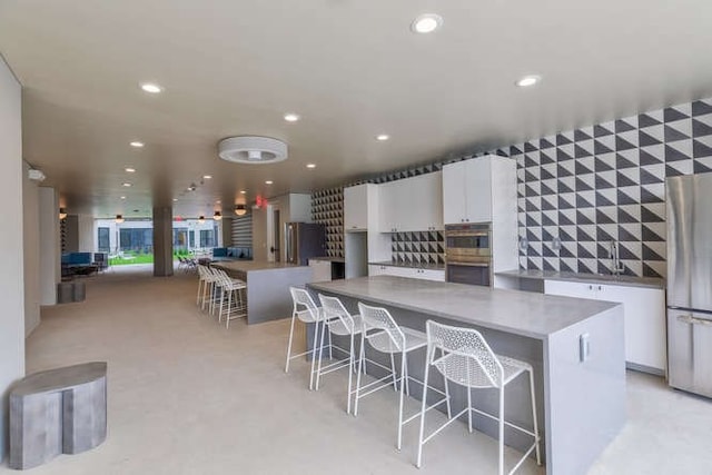 kitchen featuring a kitchen island, white cabinetry, stainless steel fridge, a kitchen bar, and fridge